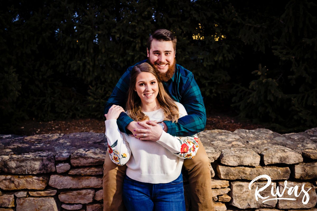 A colorful, candid picture of a couple sitting on a stone wall outside Kansas City's Nelson Atkins Museum of Art during their engagement session. 