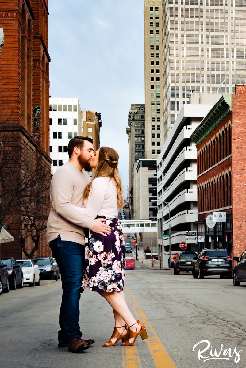 A candid picture of an engaged couple pausing in the middle of a Kansas City street for  kiss during their engagement session. 