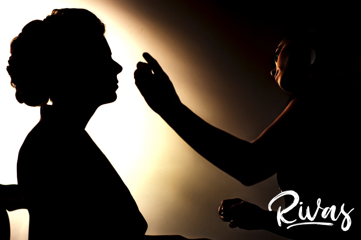 A silhouetted picture of a make-up artist applying make-up to a bride on the morning of her wedding. 