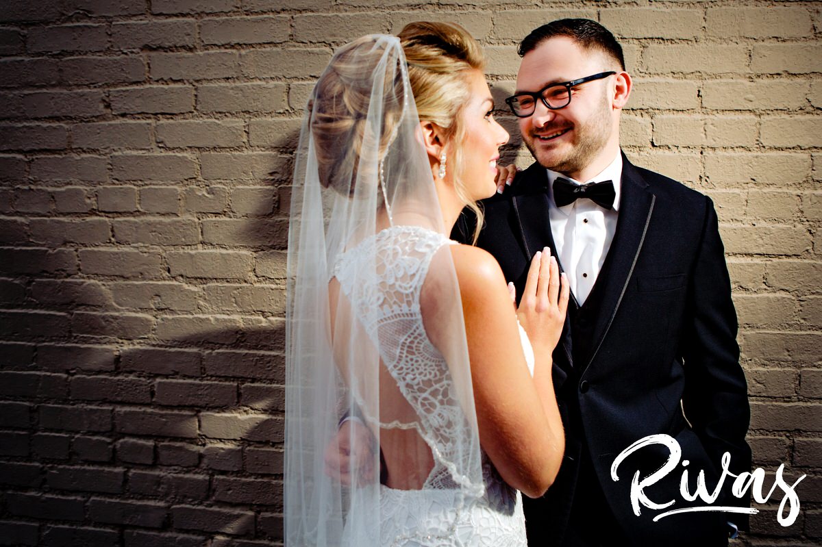 A portrait of a bride and groom leaning up against a cream brick wall in downtown Lee's Summit on the day of their winter wedding at The Stanley. 