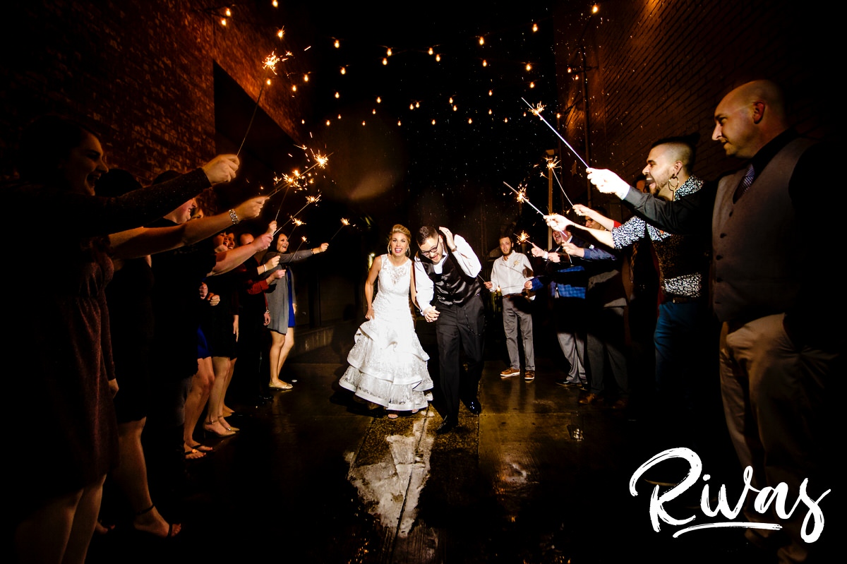 A candid picture of a bride and groom running through the rain and rain puddles underneath an arc of sparklers on their winter wedding day at The Stanley. 