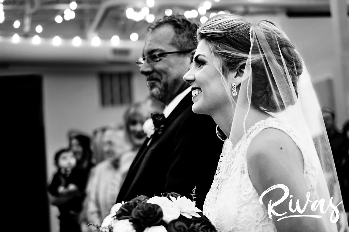 A candid, black and white picture of a bride and her father standing at the front of the aisle during her winter wedding at The Stanley in downtown Lee's Summit. 