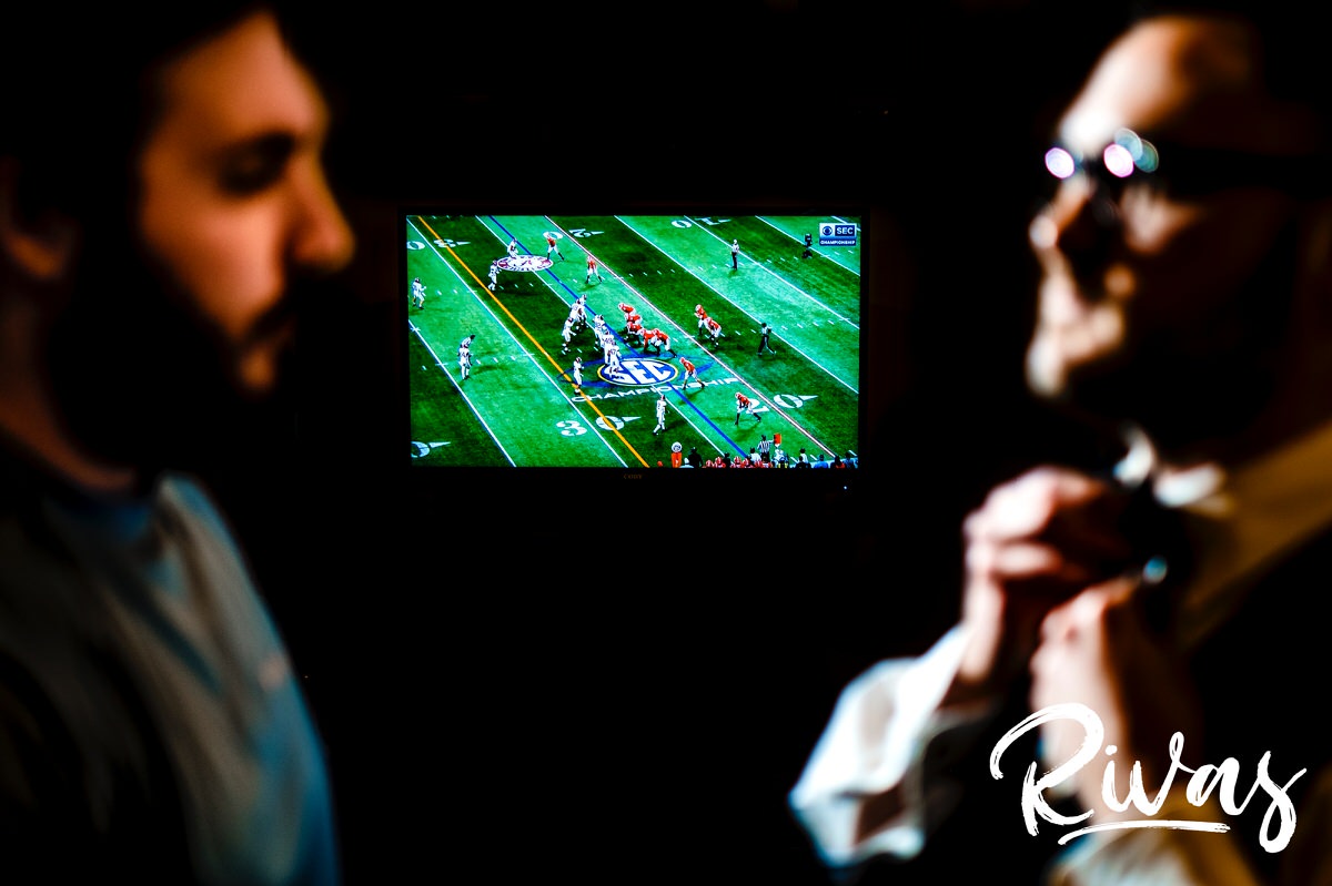 A candid, reverse focus picture of a groom adjusting his bow-tie as a football game plays on TV in the background of The Stanley's groom's suite on the morning of his winter wedding. 