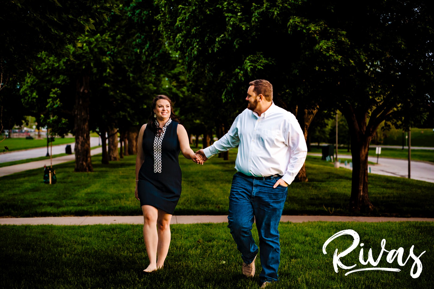 A colorful, candid picture of an engaged couple walking underneath a canopy of trees on-location during their engagement session at Liberty Memorial. 