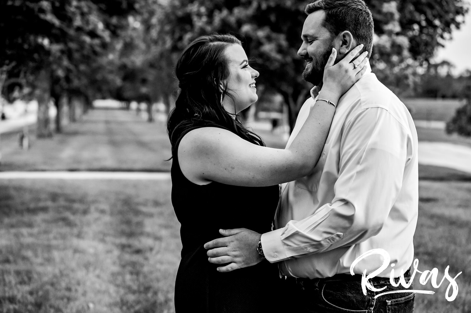A black and white picture of an engaged couple sharing an embrace as they stand in front of sun setting during their engagement session on location at Liberty Memorial. 