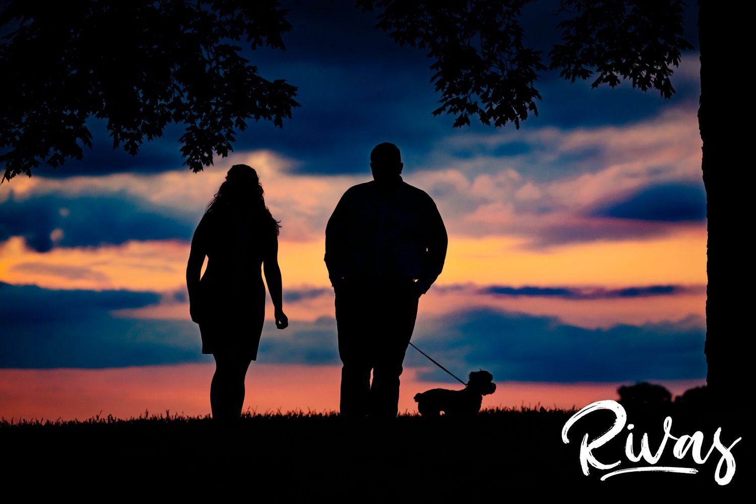 A colorful picture of an engaged couple sharing an embrace as they stand in front of sun setting during their engagement session on location at Liberty Memorial. 