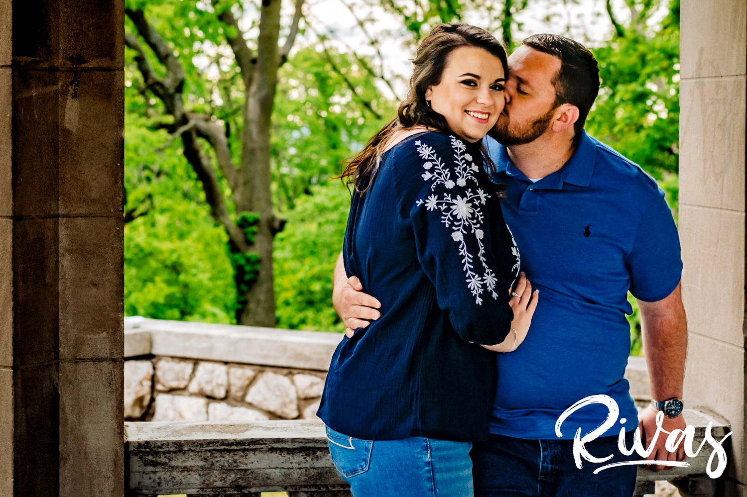 A candid picture of an engaged couple sharing a kiss and playing with their puppy during their Kansas City engagement session. 