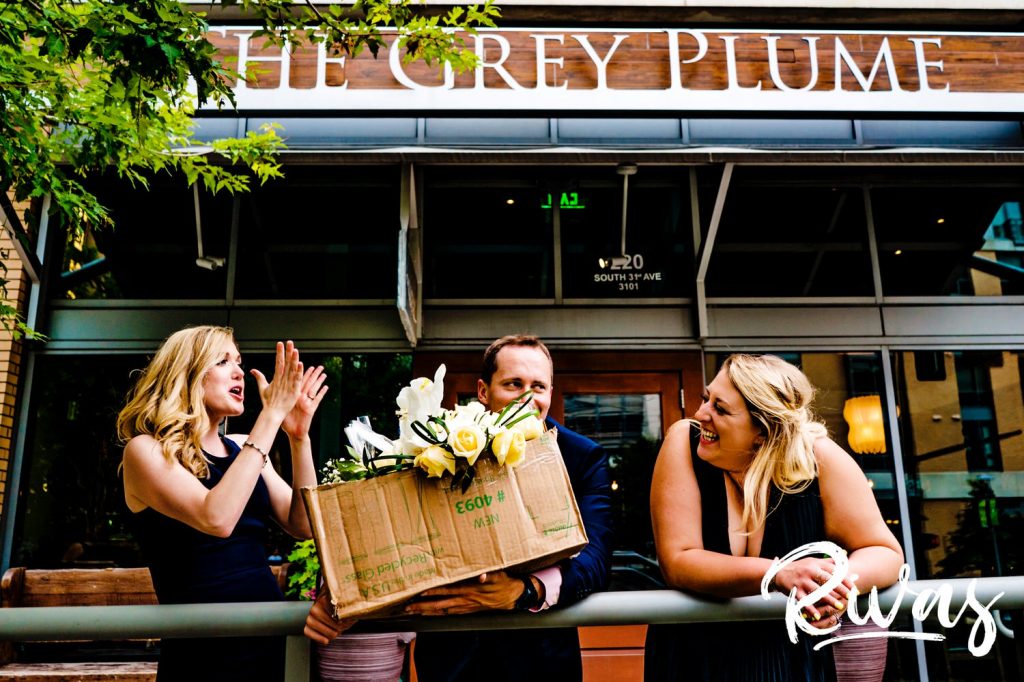 A silly picture of a bride's three adult children holding a box of flowers outside The Grey Plume in Omaha, NE. 