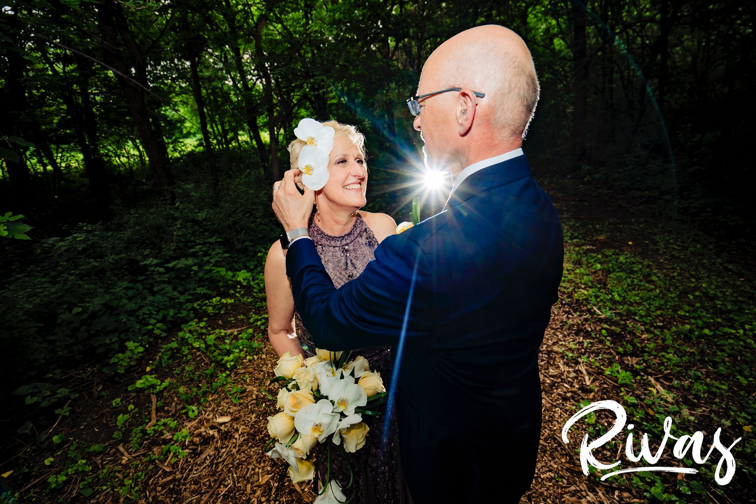 A candid picture of a groom sticking a stem of orchids behind his bride's ear just after their wedding ceremony at the Omaha OPPD Arboretum. 