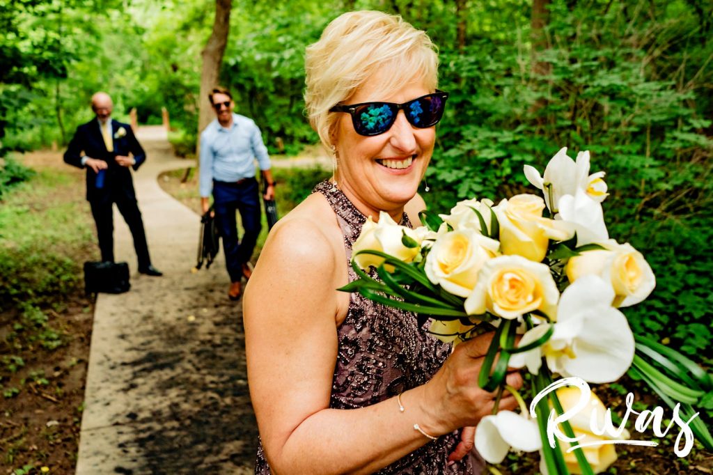 A silly, candid picture of a woman holding her bouquet of yellow roses and white orchids on her wedding day at the OPPD Arboretum in Omaha. 