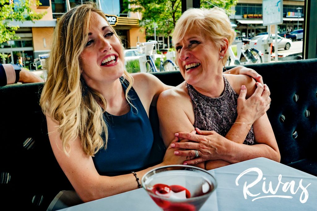 A candid, sweet moment as a mother laughs with and embraces one of her daughters during her celebratory wedding dinner at The Grey Plume in Omaha. 