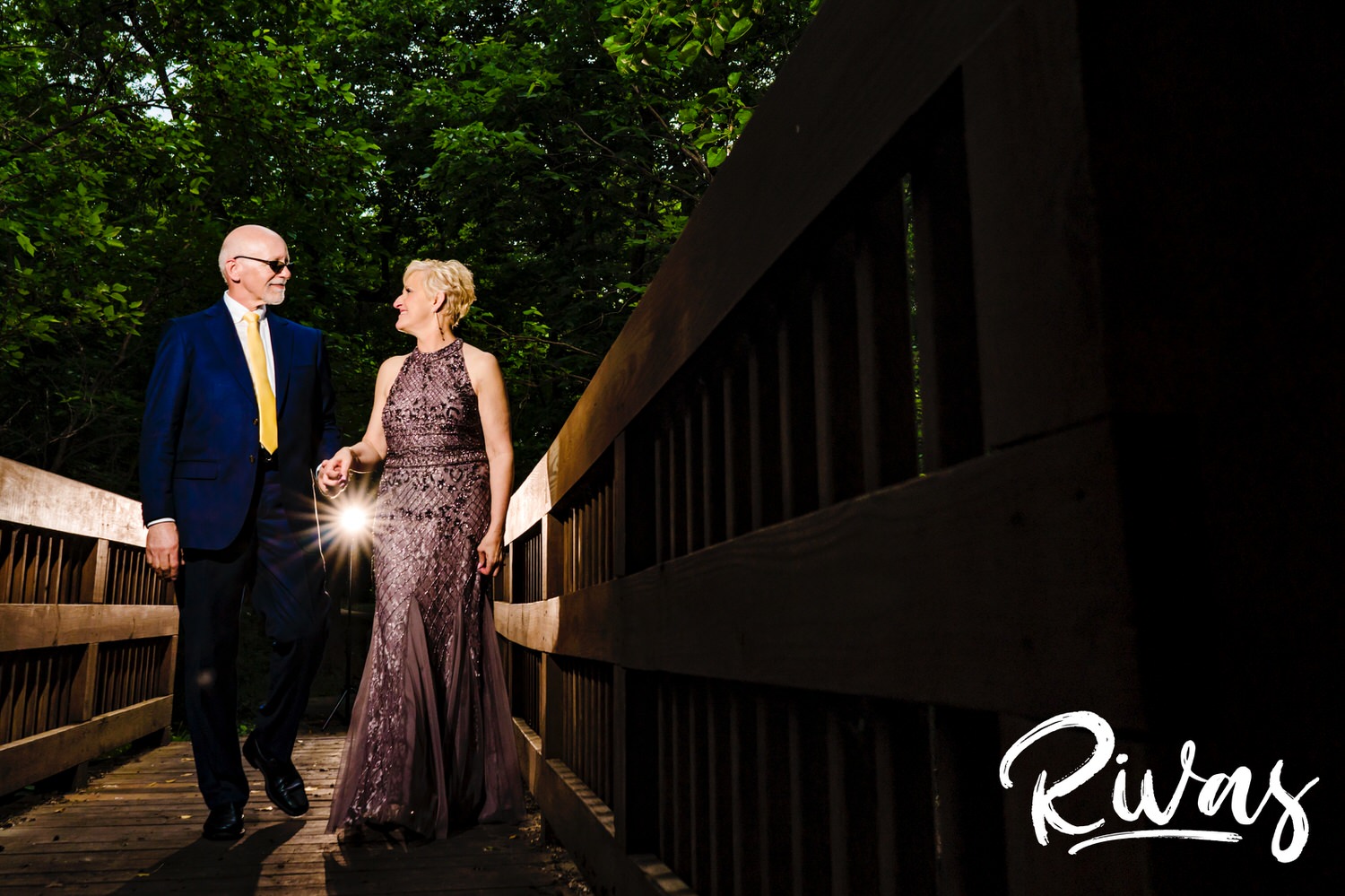 A candid picture of a man and woman holding hands and walking across a bridge at Omaha's OPPD Arboretum on their wedding day. 