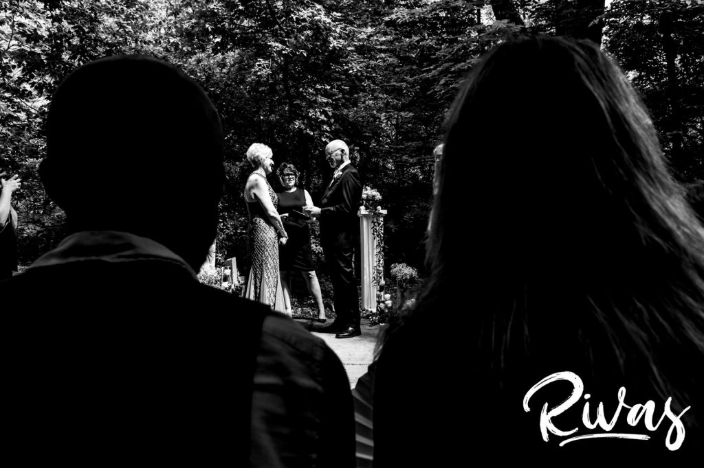 A black and white image taken from behind the attendees of an intimate wedding ceremony in Omaha at the OPPD Arboretum. 