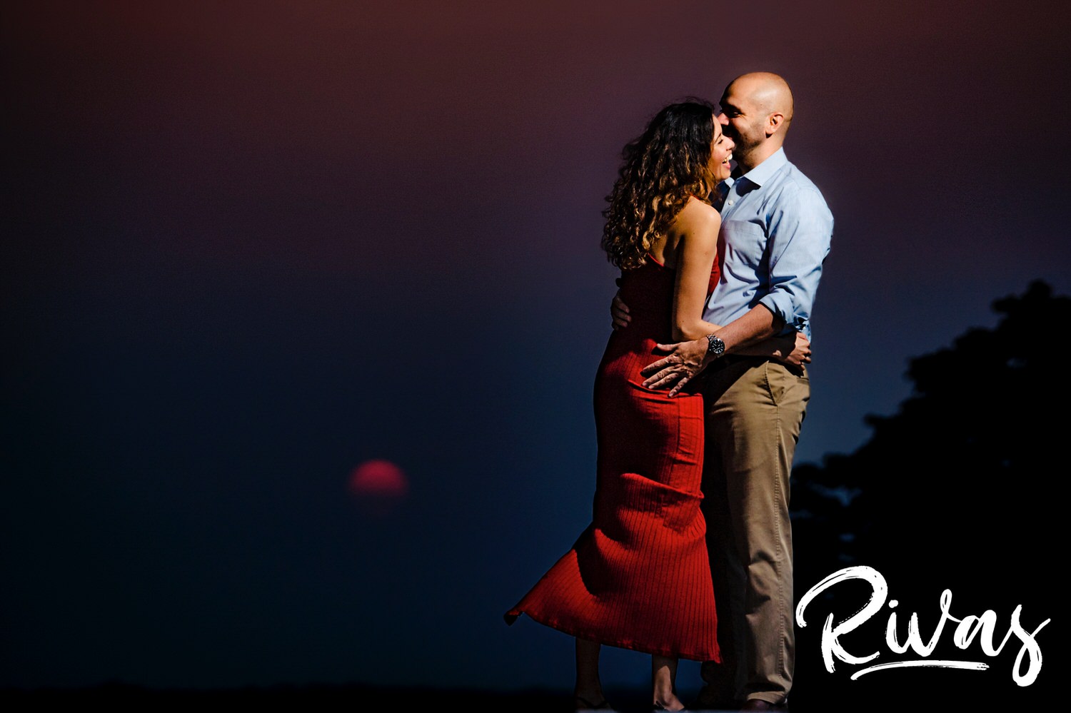 A candid picture of an engaged couple dancing together at Liberty Memorial with the pink sun setting in the background. 