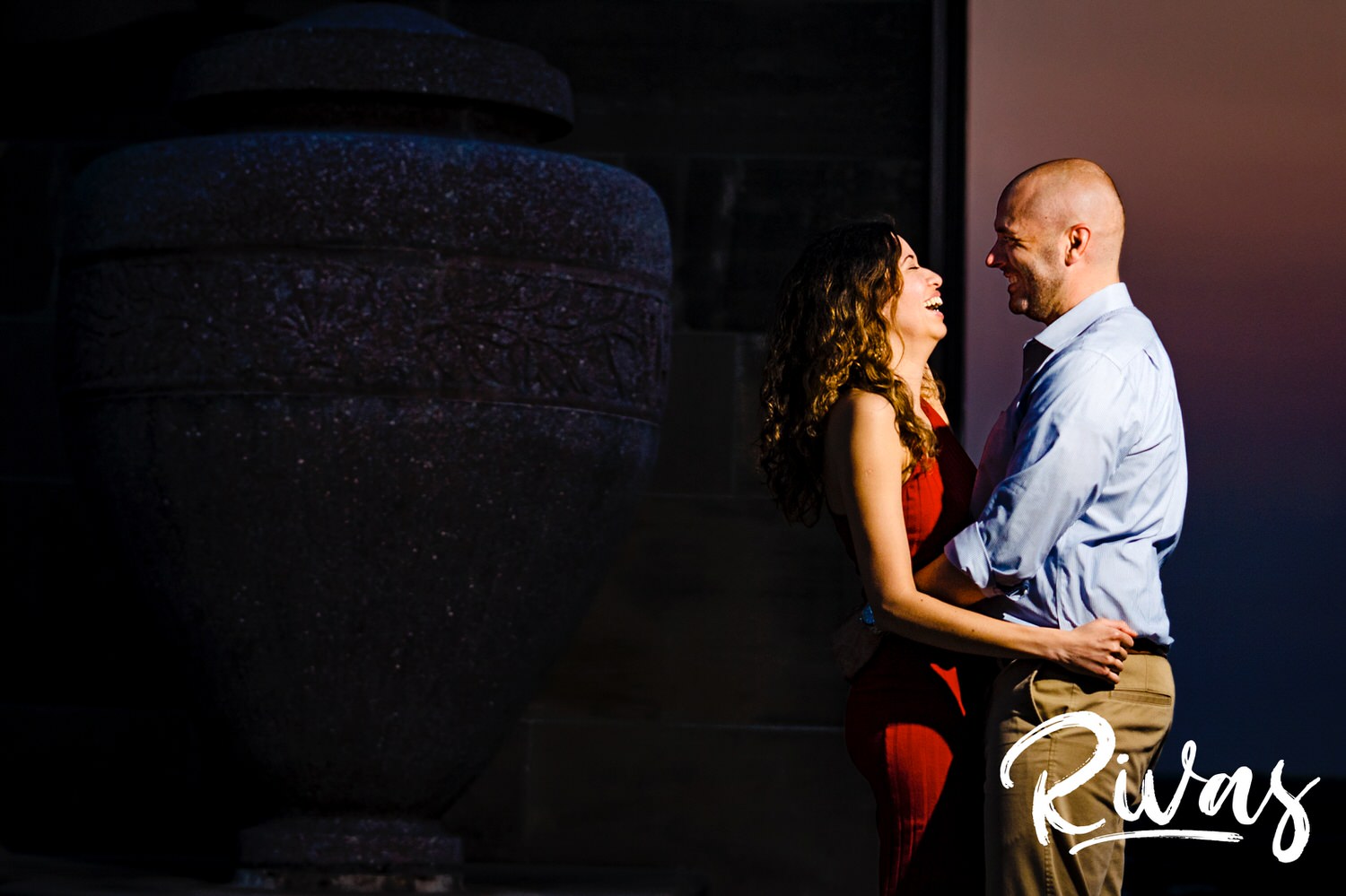 A candid picture of an engaged couple sharing an embrace and laughing together as the sun sets behind them at Liberty Memorial. 
