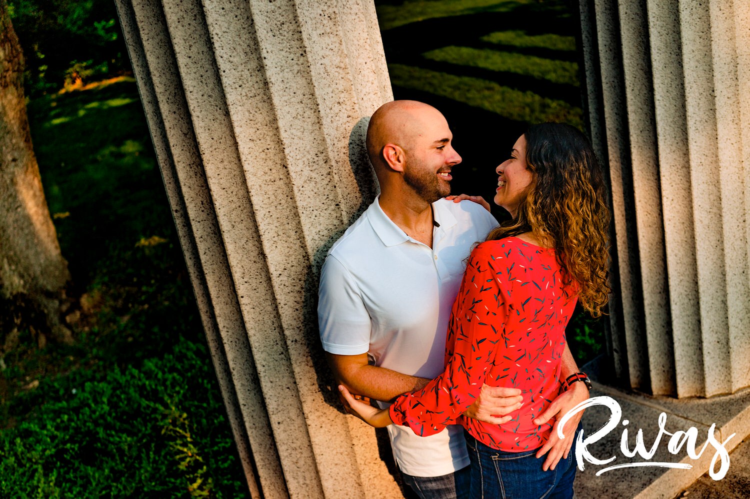A bright, candid portrait of a man leaning up against a column as he looks lovingliy into his partner's eyes during their KC engagement session. 