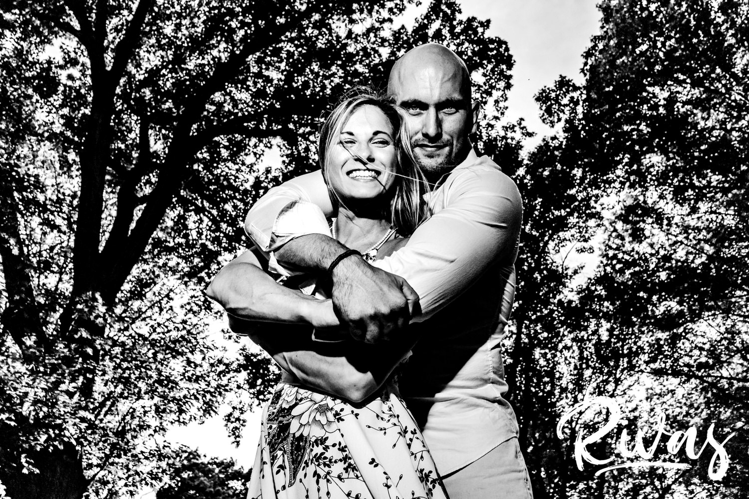 A candid black and white portrait of an engaged couple sharing an embrace and looking at the camera during their Loose Park Engagement Session. 