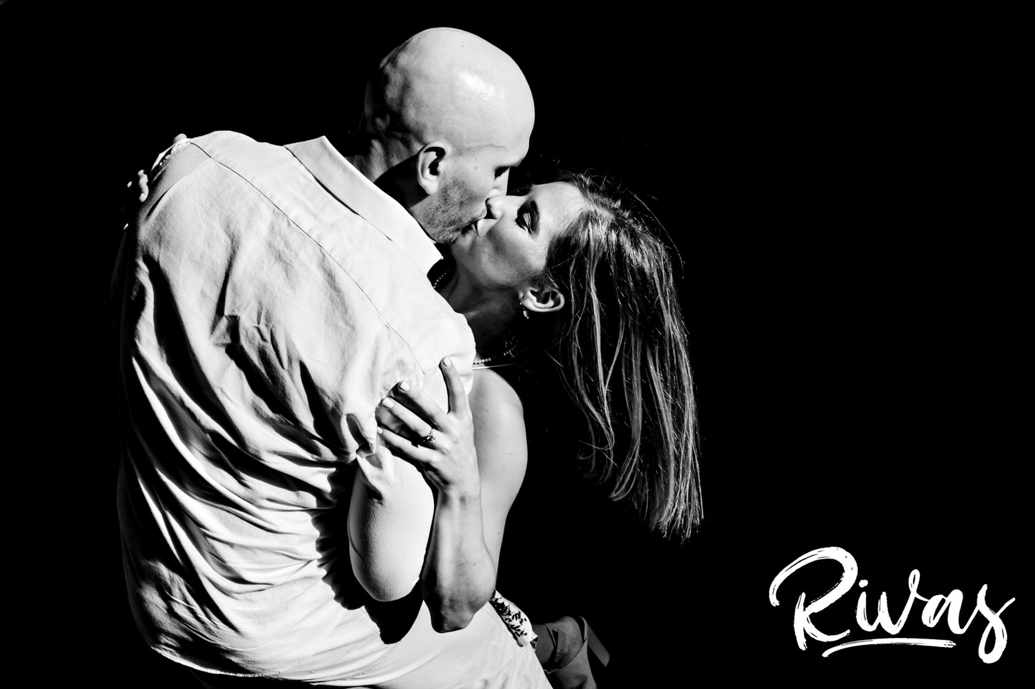 A dramatic, black and white picture of an engaged couple sharing a kiss against an otherwise black background during their engagement session in Kansas City. 