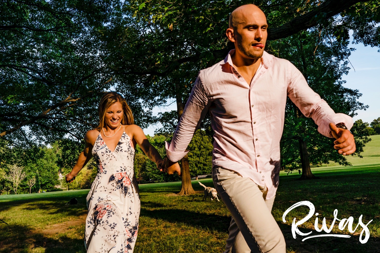 A candid picture of an engaged couple holding hands and running into the sunlight during their Loose Park Engagement Session. 