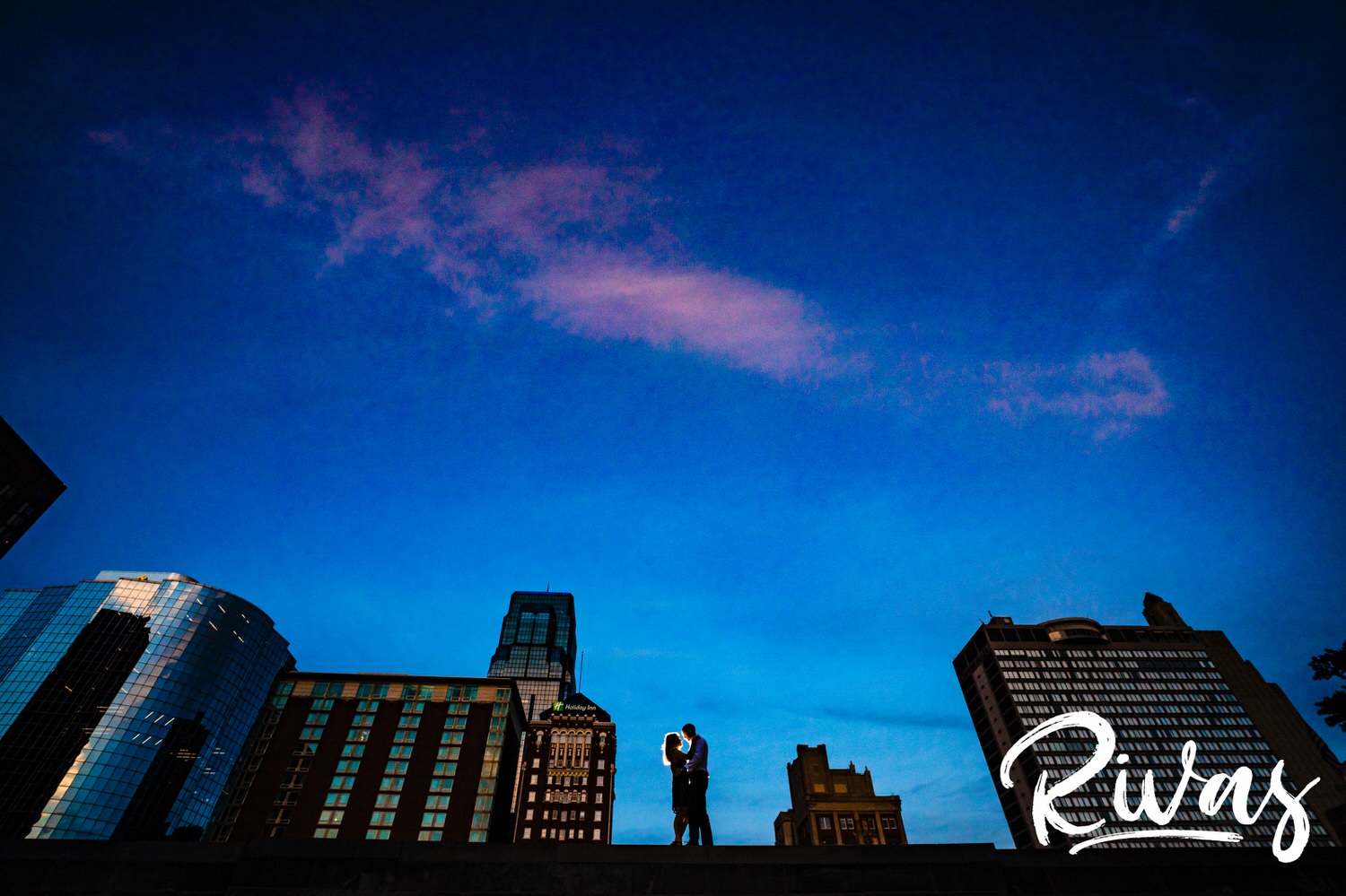 A very wide, vibrant, silhouetted portrait of an engaged couple standing in a gap of the Kansas City skyline during their engagement session in Kansas City. 