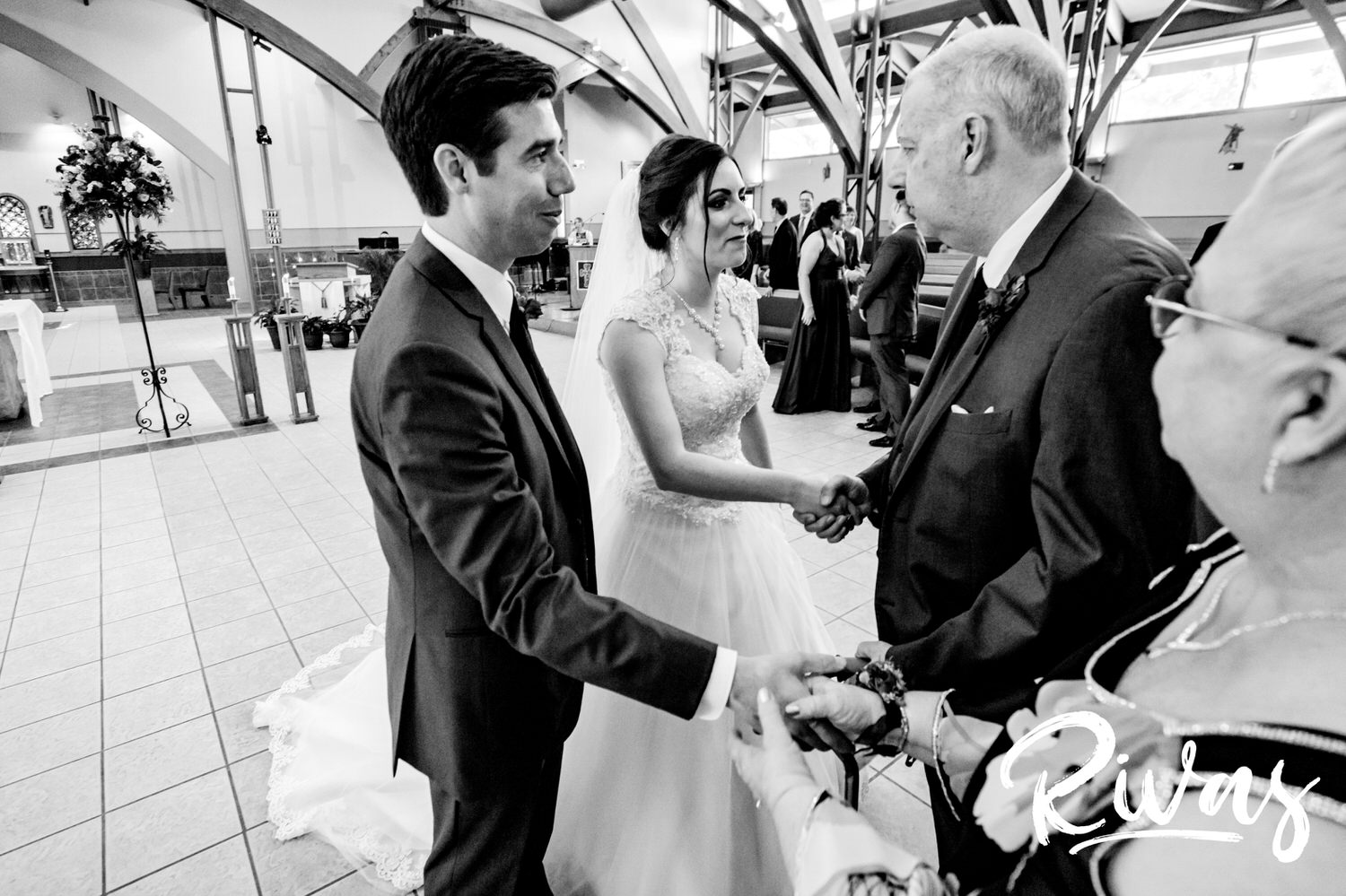 A candid black and white picture of a bride and groom greeting the groom's parents during a Catholic mass wedding ceremony,. 