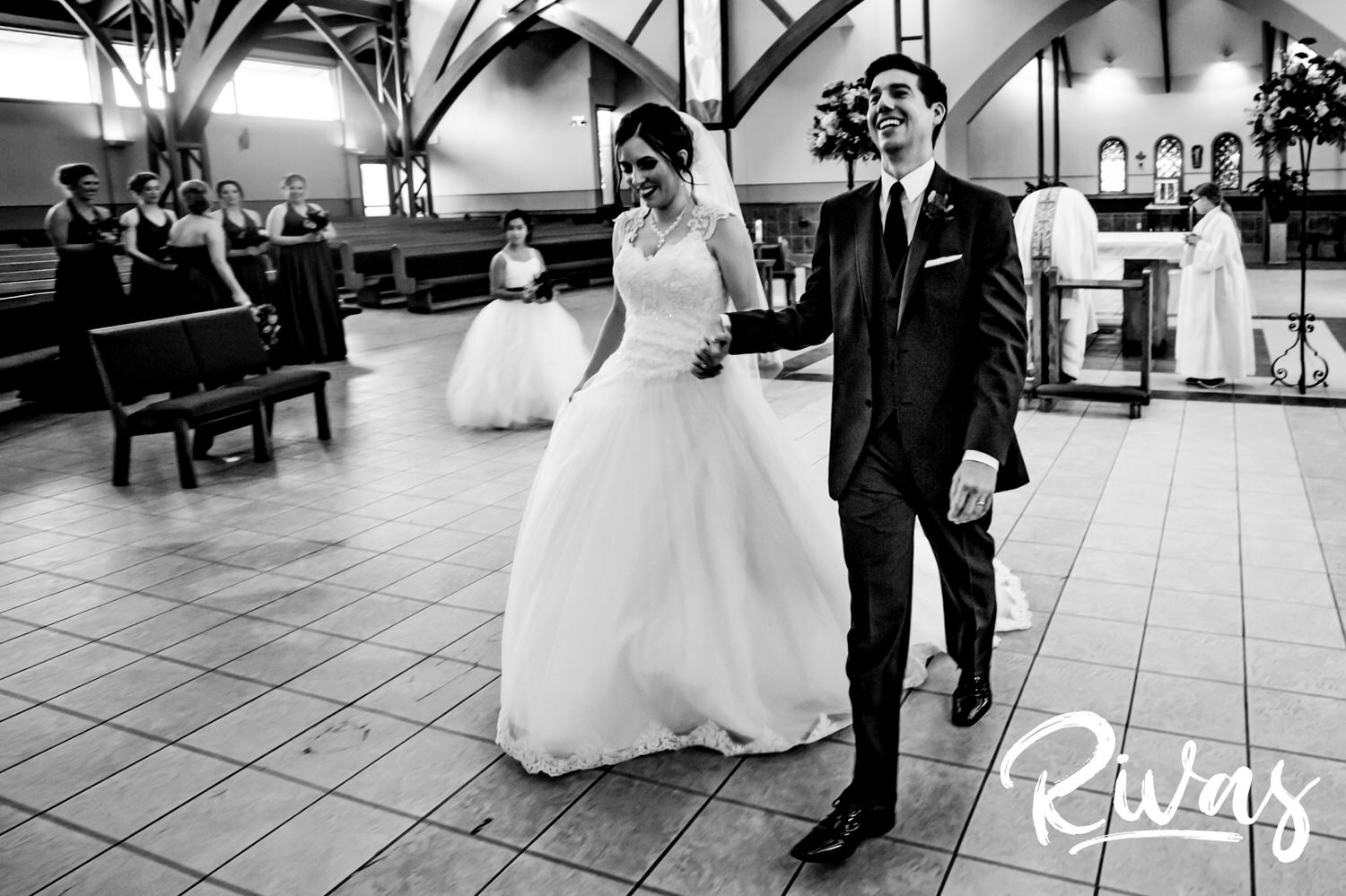 A candid black and white picture of a bride and groom holding hands and walking towards the back of the church after their wedding ceremony. 