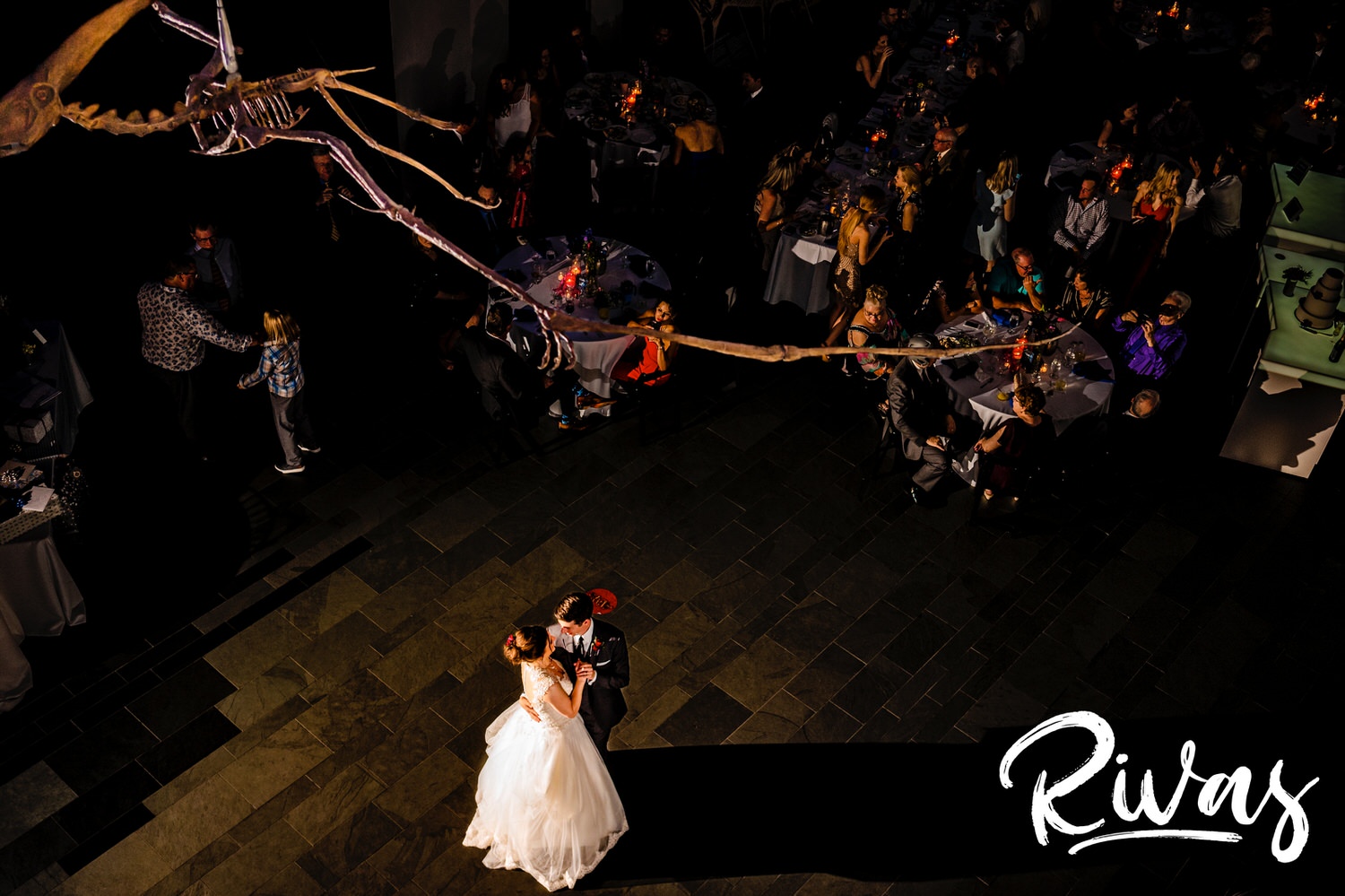 A candid picture taken from a balcony looking down of a bride and groom sharing their first dance during their wedding reception at The Museum at Prairiefire in Kansas City. 