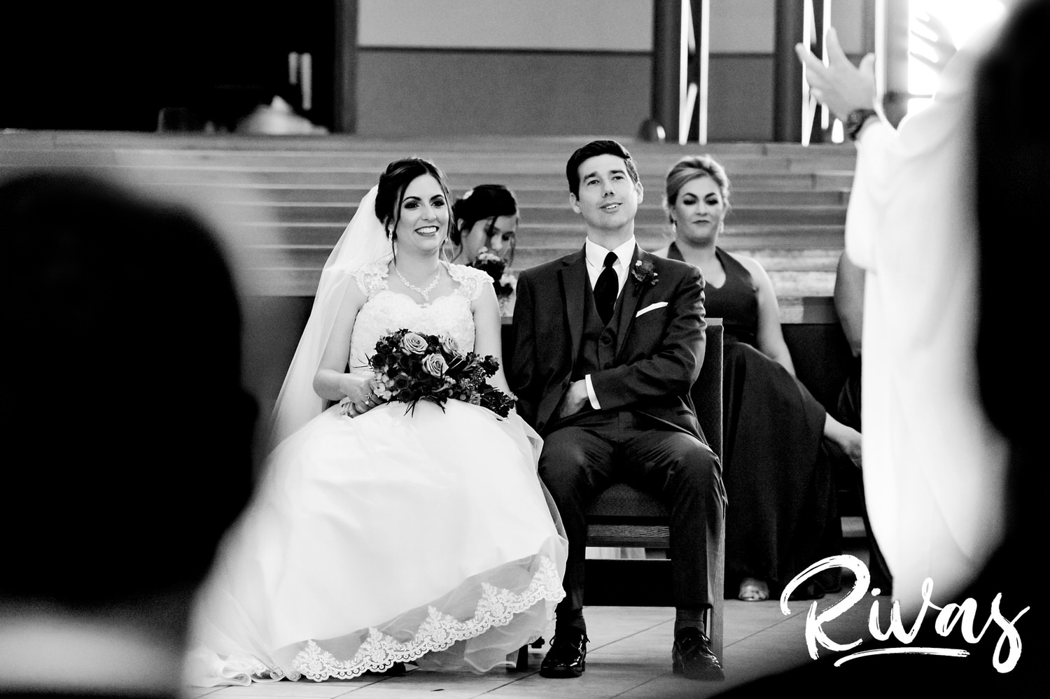A candid black and white picture of a bride and groom sitting and watching their officiate during their wedding ceremony. 