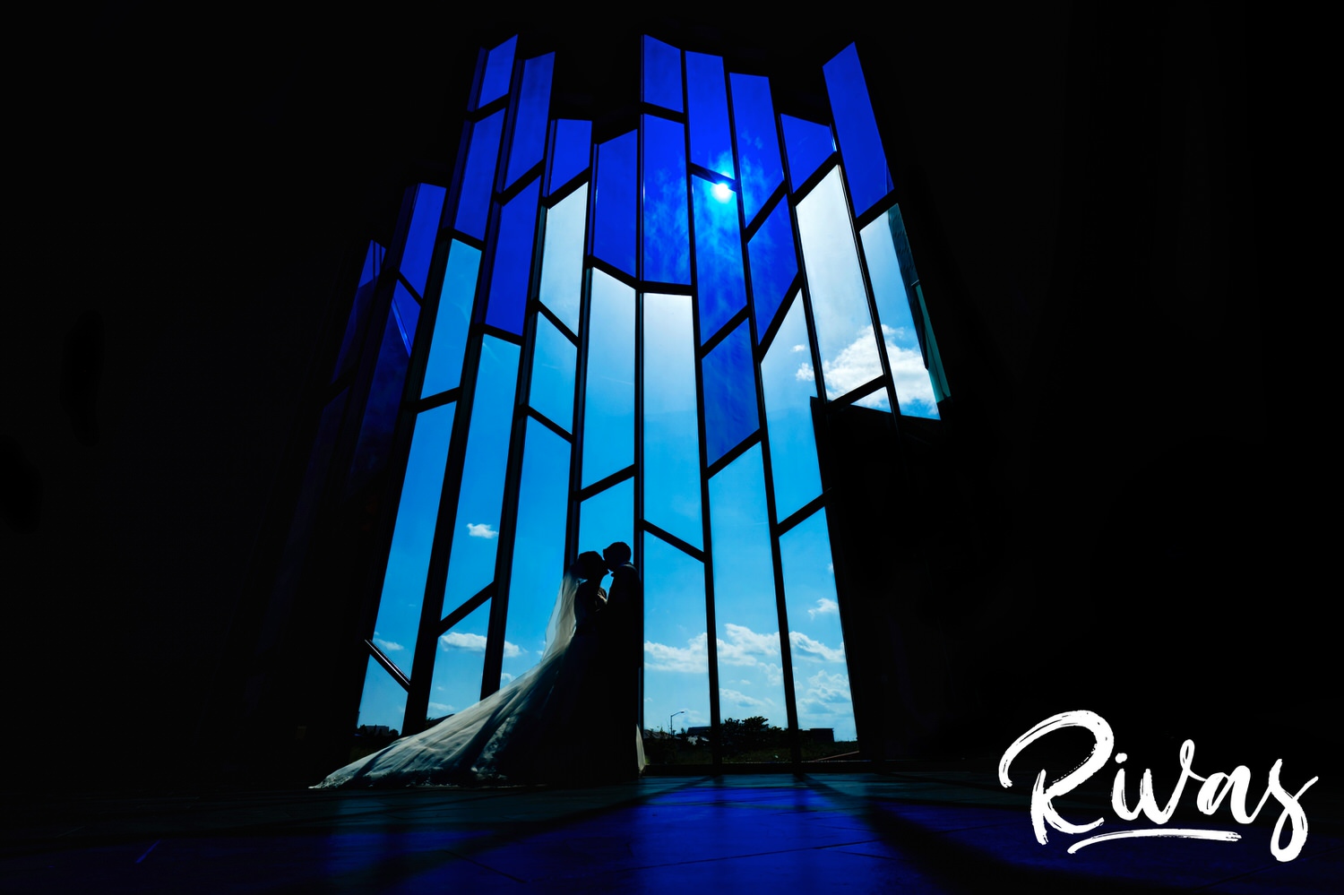 A vibrant, bold portrait of a bride and groom sharing a kiss silhouetted in front of the large stained glass windows at the Museum at Prairiefire on their wedding day. 