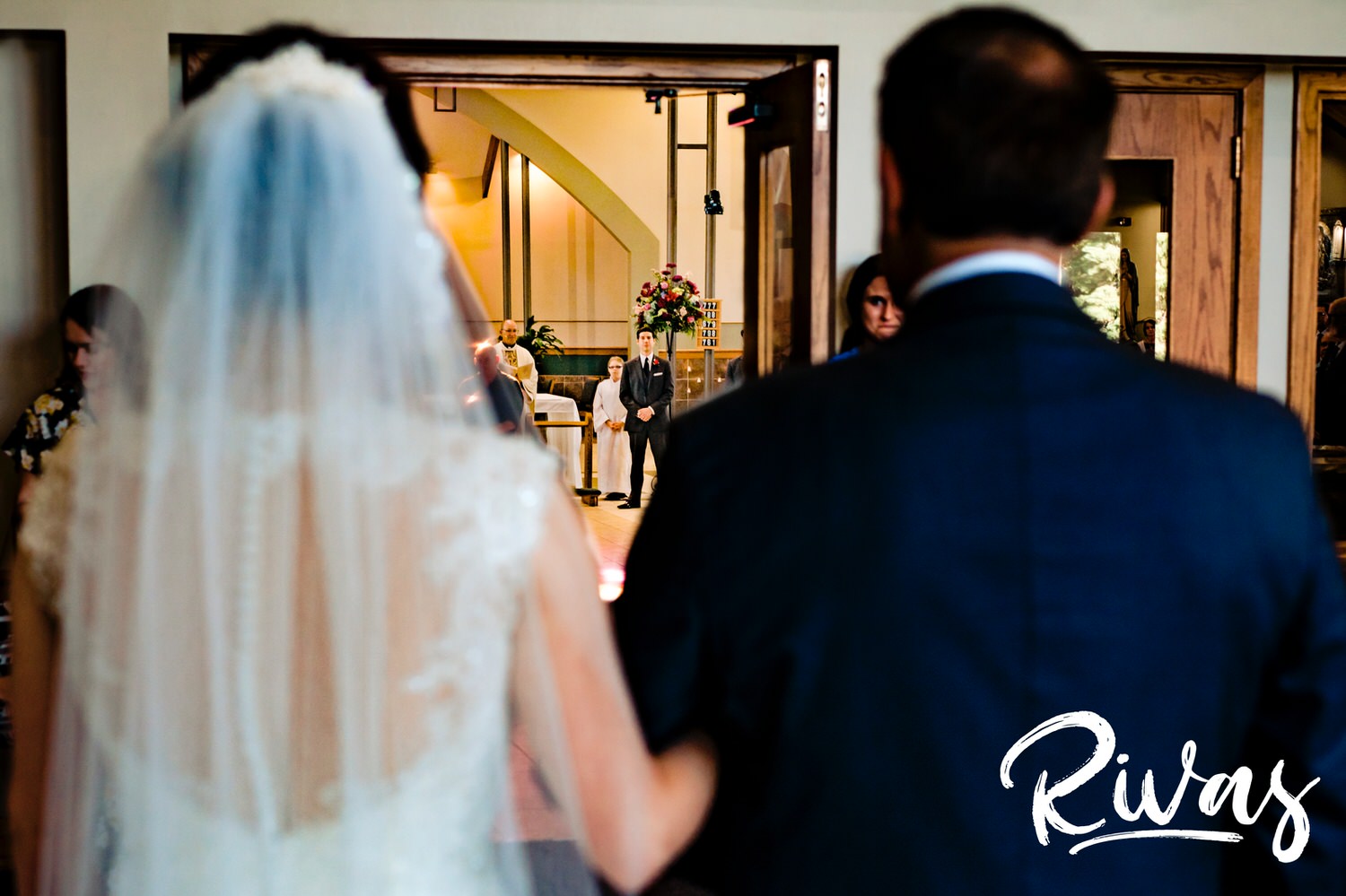 A candid picture taken over the bride's shoulder of her groom at the front of the church as she walks into a church sanctuary on her KC wedding day. 