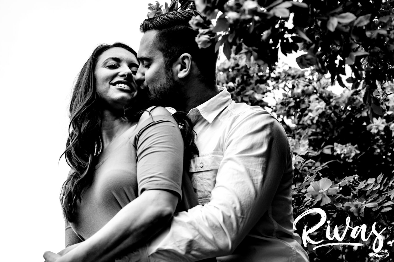 A black and white picture of an engaged couple wrapped up in each others' arms during their summer engagement session at Loose Park in Kansas City.