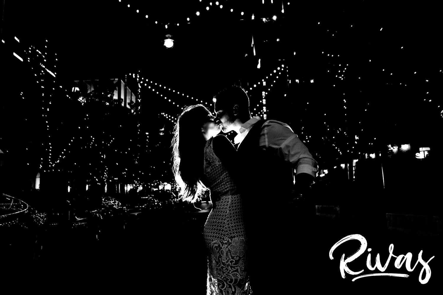 A dramatic, black and white picture of an engaged couple sharing a kiss as they stand in the middle of the street in Kansas City's Power & Light District during their summer engagement session. 