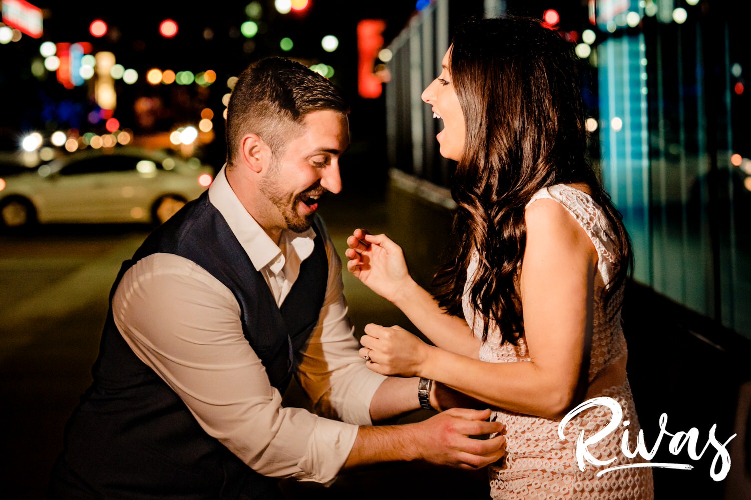 A colorful, candid picture taken after dark of a man tickling a woman as she laughs hysterically during their summer engagement session in downtown Kansas City.