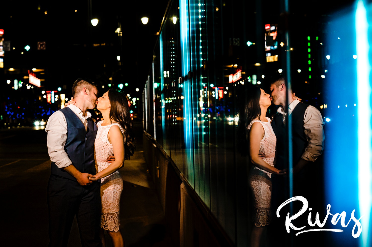 A colorful picture of an engaged couple sharing a kiss just after dark during their summer engagement session in downtown Kansas City. 