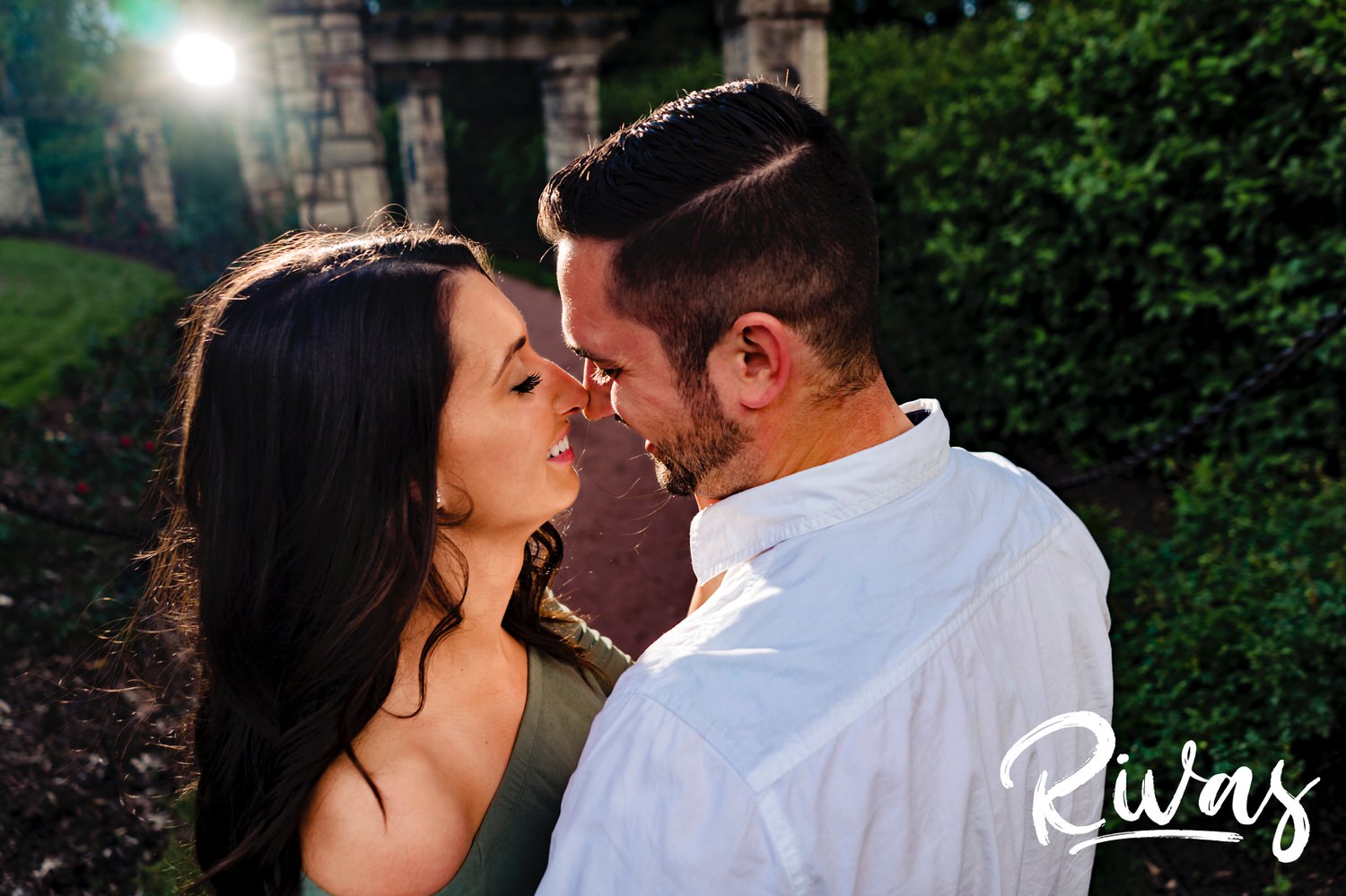 A candid picture of an engaged couple leaning in to share a kiss during their summer engagement session at Kansas City's Loose Park. 