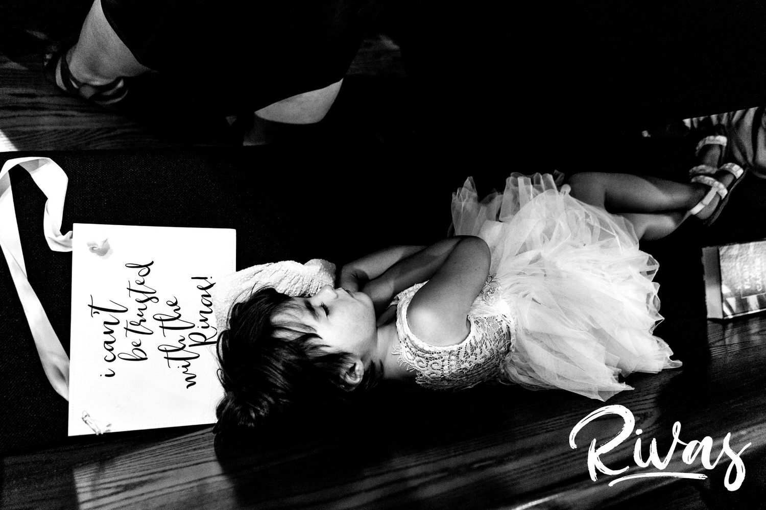 A candid black and white picture of a flower girl sleeping on a sign and pew during the middle of a wedding ceremony in Kansas City. 