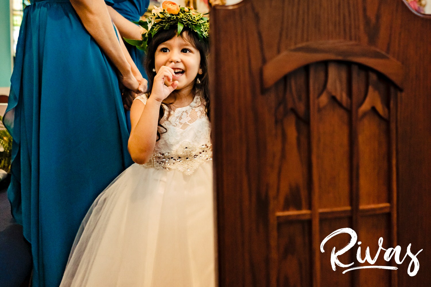 A candid picture of a flower girl in a flower crown laughing and smling during a wedding ceremony. 
