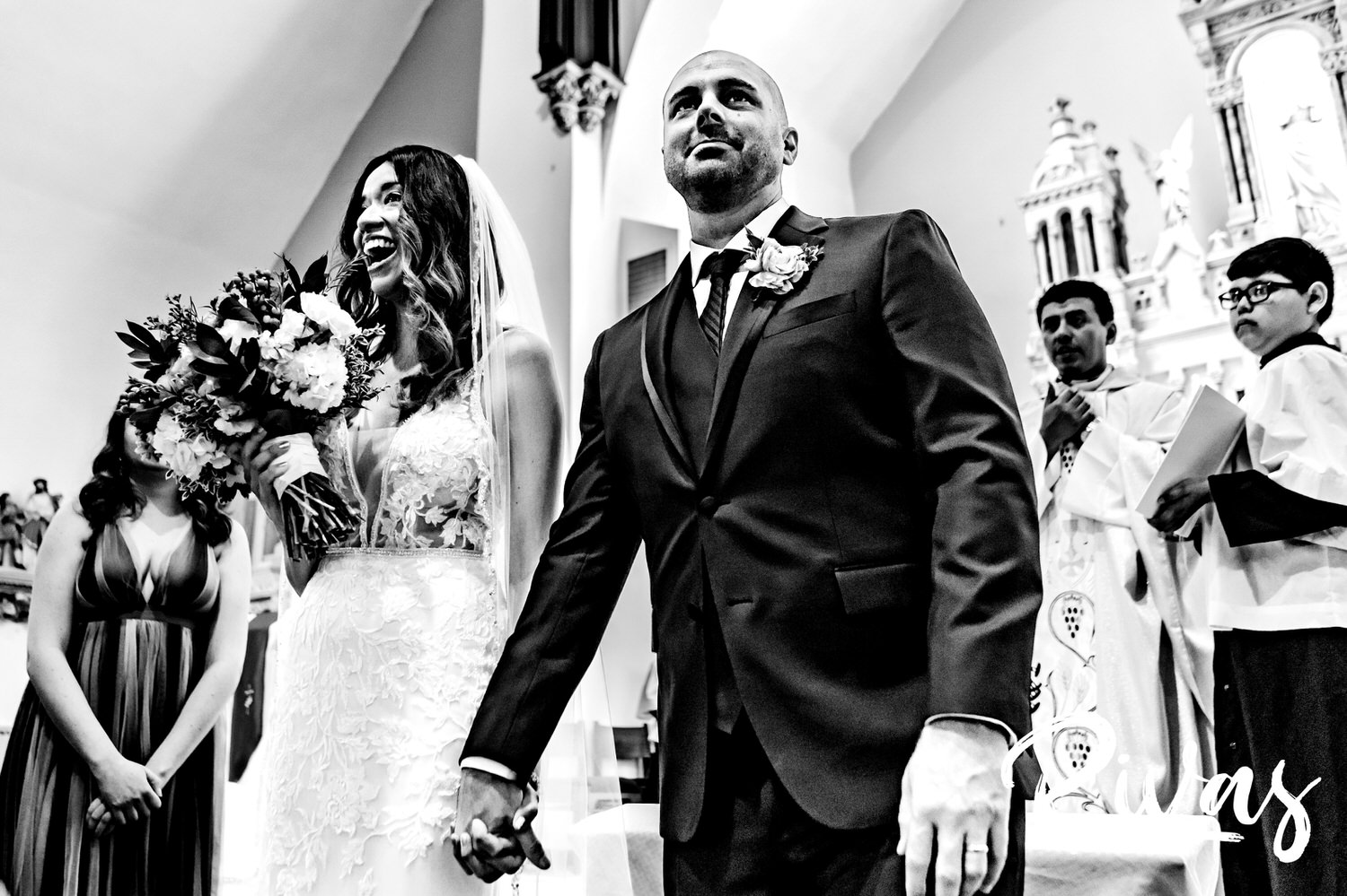 A candid black and white picture of a bride and groom holding hands in celebration after their wedding ceremony in Kansas City. 