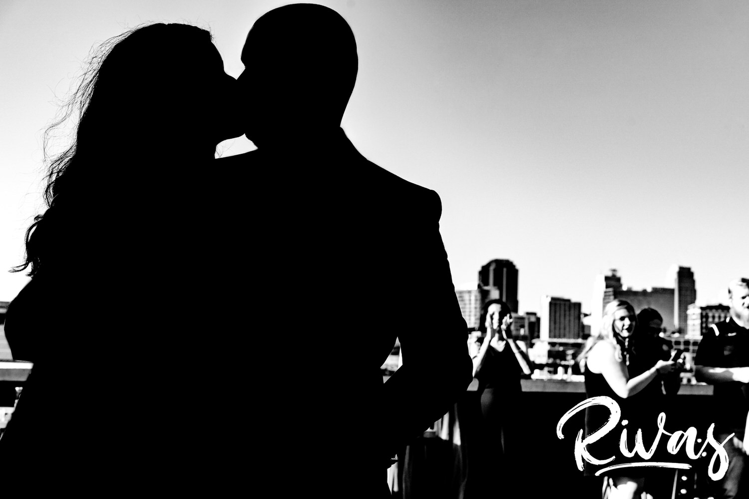 A black and white silhouette of a bride and groom leaning in for a kiss in front of the Kansas City skyline during their wedding reception. 