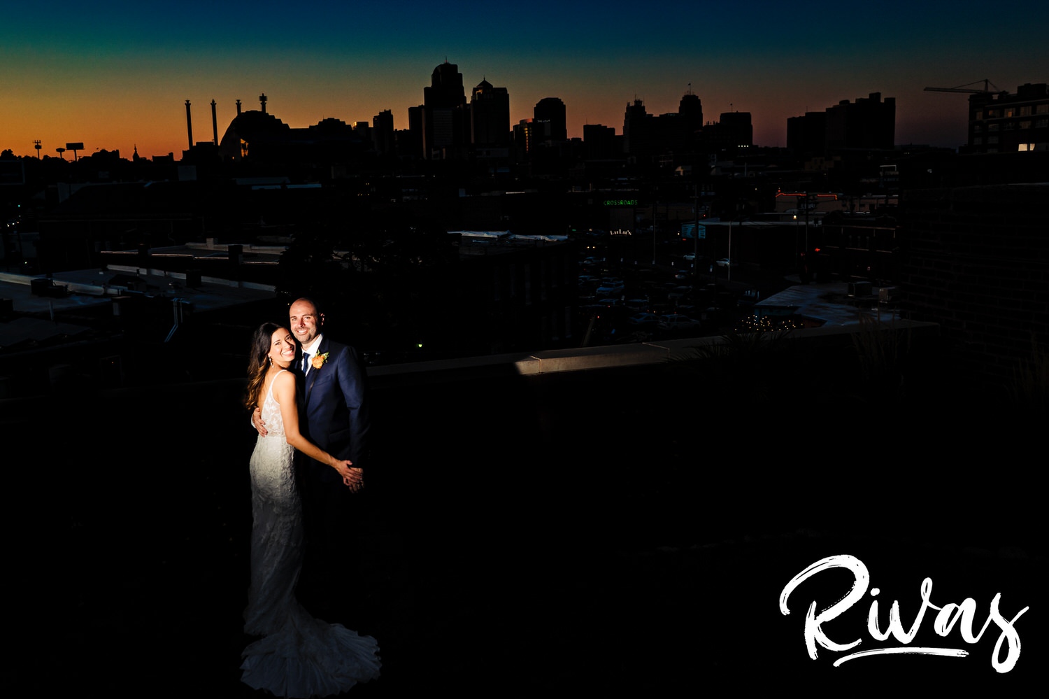 A vibrant portrait of a bride and groom in front of the Kansas City skyline at sunset during their wedding reception. 