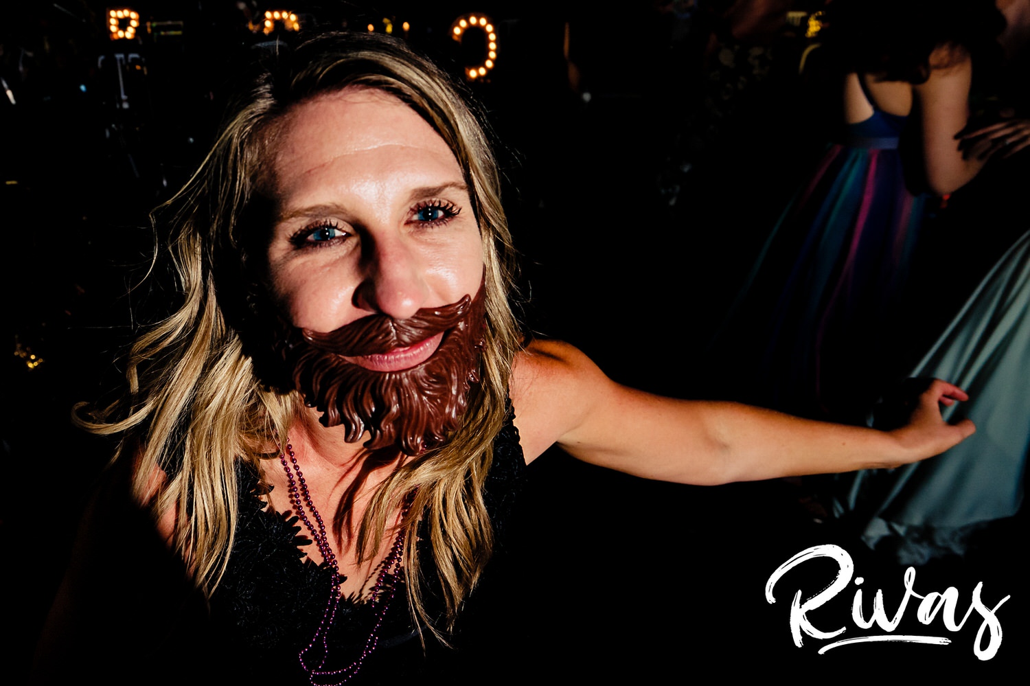 A candid, close-up picture of a blonde woman wearing a plastic beard while dancing during a wedding reception in Kansas City. 