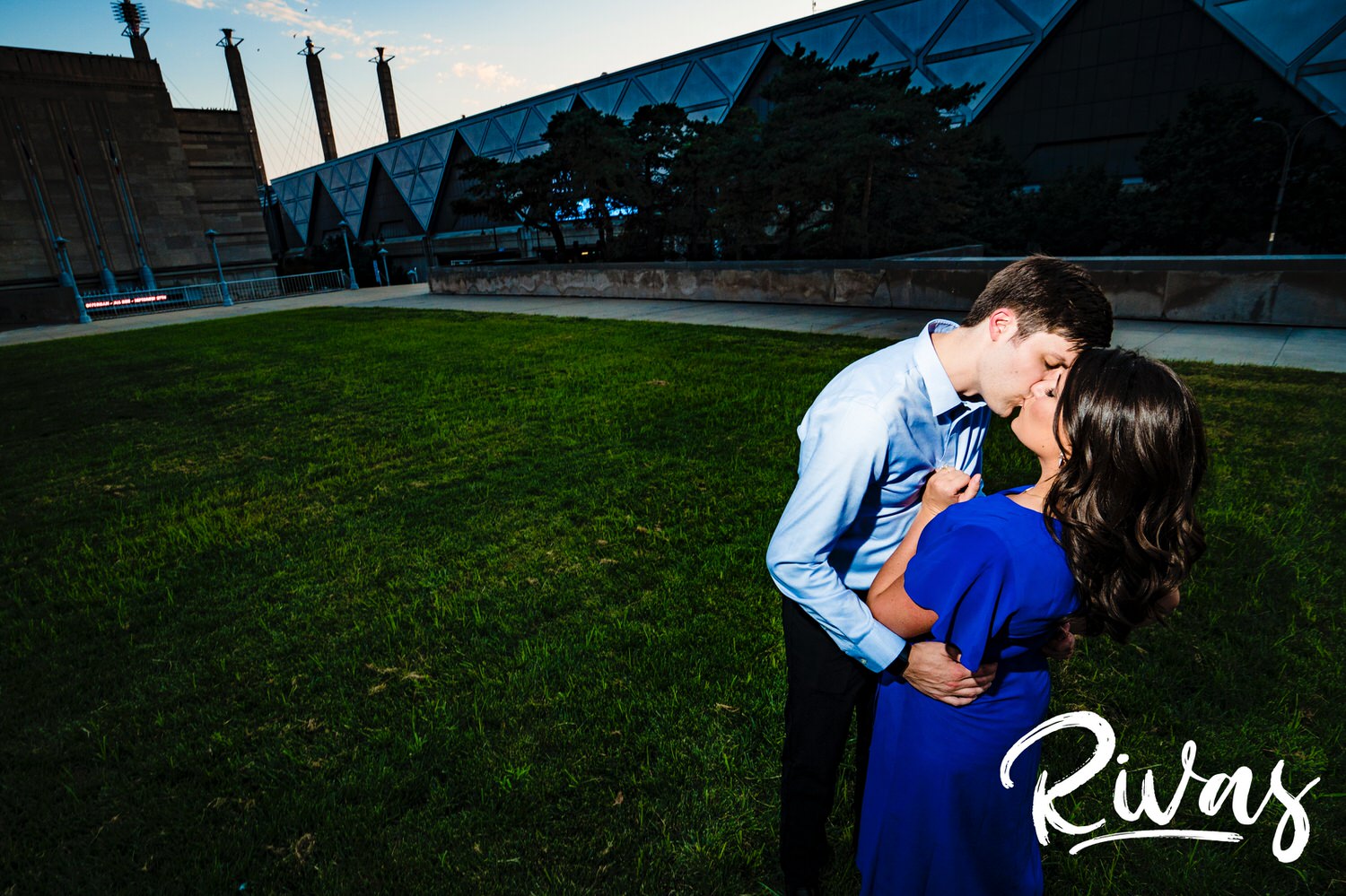 A vibrant portrait of an engaged couple standing on the side of a fountain with the Kansas City skyline visible in the background during their fall engagement session. 