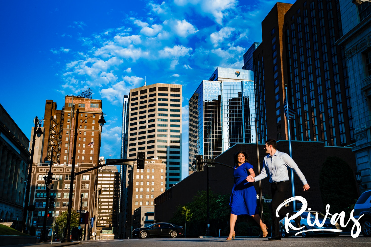 A bright, candid picture of an engaged couple holding hands as they run across a downtown Kansas City street during their fall engagement session. 
