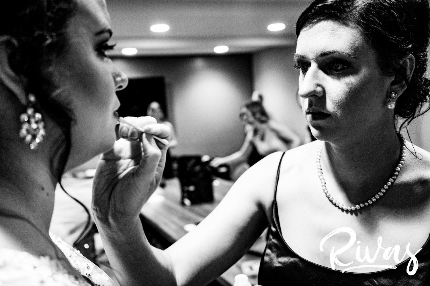 A candid black and white picture of a bridesmaid putting lipstick on the bride moments before she walks down the aisle on her wedding day in Lawrence. 