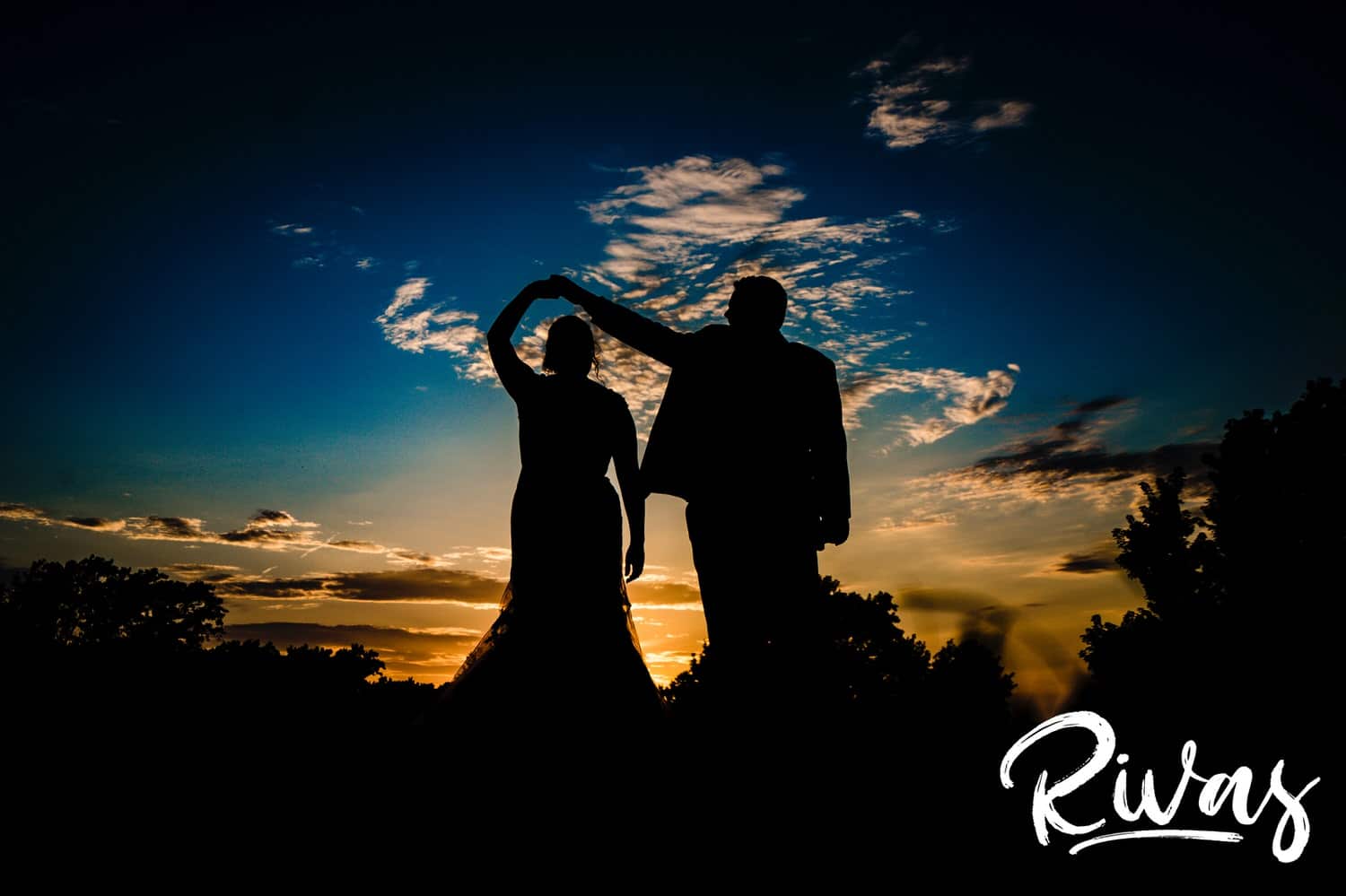 A candid, silhouetted image of a groom twirling his bride under his arm at sunset of their summer wedding day at Lawrence Country Club. 