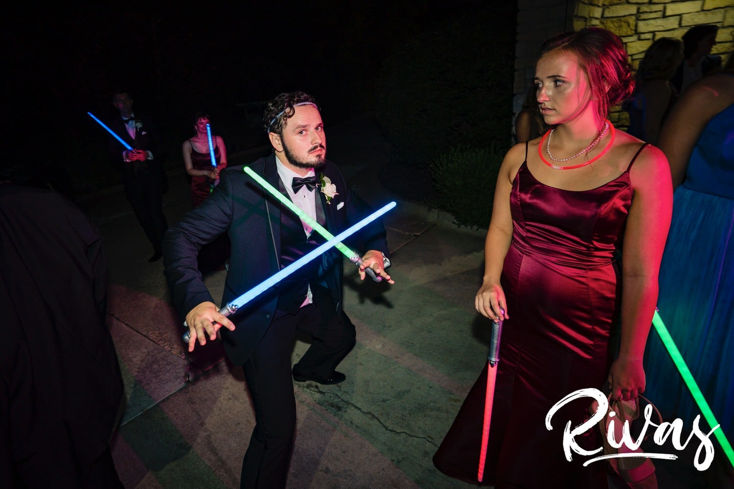 A candid picture of a groom's siblings playing with lightsabers at the end of a summer wedding day at Lawrence Country Club. 