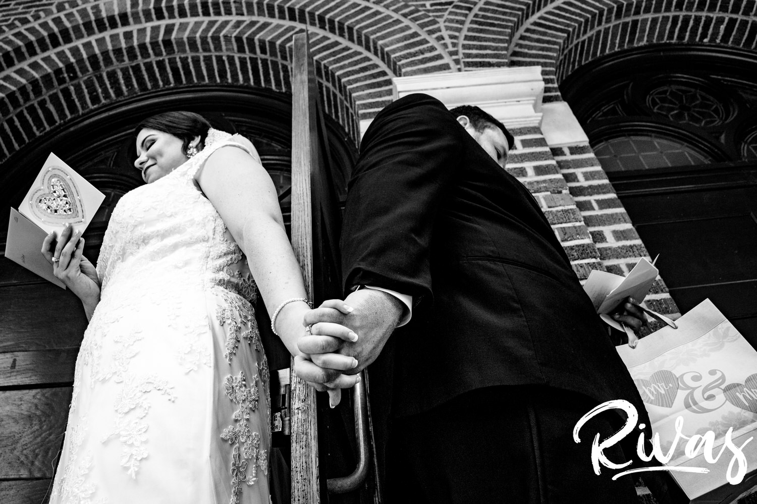 A candid black and white picture taken from below of a bride and groom holding hands around a door as they exchange gifts and letters on the morning of their wedding in Lawrence, Kansas. 
