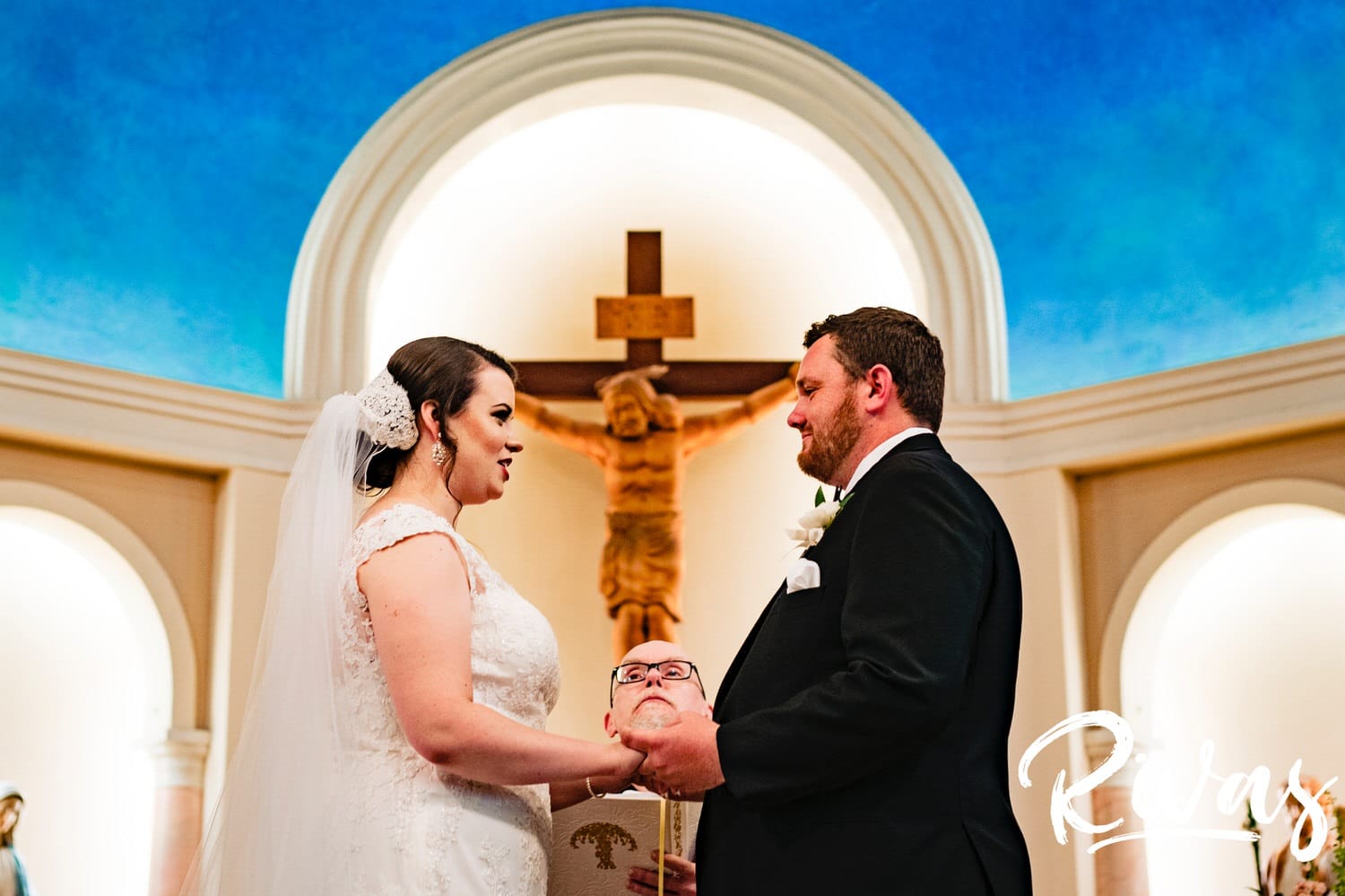 A vibrant picture of a bride and groom holding hands and smiling at each other as they exchange vows and rings during their wedding ceremony in Lawrence, Kansas. 