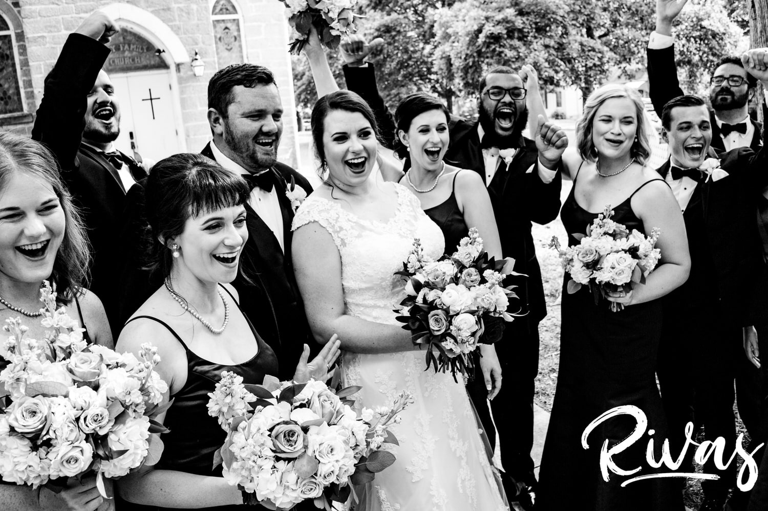 A candid black and white picture of a wedding party laughing and shouting in joy on a summer wedding day in Lawrence, Kansas. 