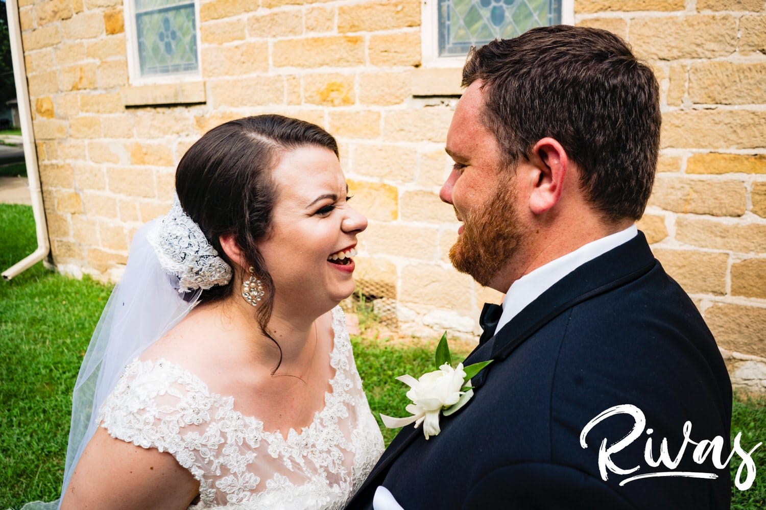 A colorful, candid picture of a bride and groom laughing together as they stand outside the church the bride's grandparents were married in on a summer wedding day in Lawrence. 